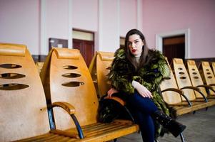 brunette meisje in groene bontjas op de stoelen in de wachtkamer op het station. foto