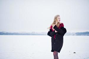 elegantie blond meisje in bontjas en rode avondjurk gesteld op besneeuwde winterdag. foto