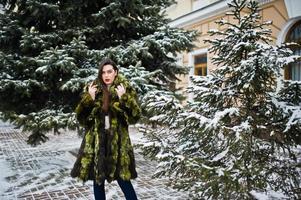 brunette meisje in groene bontjas op winterdag tegen besneeuwde dennenboom. foto