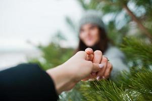 portret van zacht meisje in grijze jas en hoed tegen nieuwjaarsboom buiten hand in hand. foto