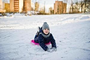 schattig klein meisje met schotel sleeën buiten op winterdag. foto