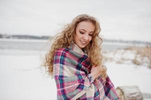 krullend blond meisje in geruite plaid tegen bevroren meer op winterdag. foto