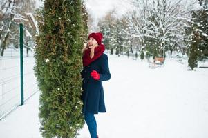 blond meisje in rode sjaal en jas wandelen in het park op winterdag. foto