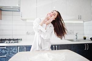 brunette meisje, draag shirt en ondergoed, speel met bloem in de witte keuken. foto