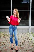 portret van een aantrekkelijke jonge vrouw poseren met koffie en smartphone buiten het winkelcentrum. foto