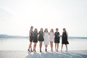 groep van 7 meisjes dragen op zwart en 2 bruiden op vrijgezellenfeest tegen zonnig strand. foto