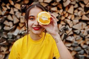 jong grappig meisje met lichte make-up, draag op geel shirt, houd picece van oranje tegen houten achtergrond. foto