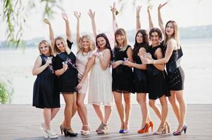 groep van 8 meisjes dragen op zwart en 2 bruiden op vrijgezellenfeest tegen zonnig strand champagne drinken. foto