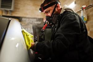 man in uniform en gasmasker, werknemer van autowascentrum, auto-interieur schoonmaken met hete stoomreiniger. auto detaillering concept. foto