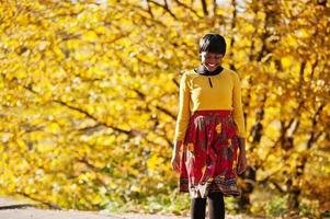 Afrikaans Amerikaans meisje bij gele en rode jurk in het gouden herfstpark. foto