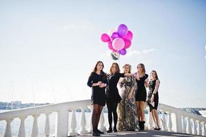 vijf meisjes dragen op zwart wandelen met ballonnen op vrijgezellenfeest tegen meer. foto