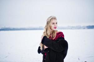 elegantie blond meisje in bontjas en rode avondjurk gesteld op besneeuwde winterdag. foto