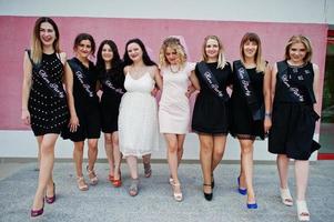 groep van 8 meisjes dragen op zwart en 2 bruiden op vrijgezellenfeest tegen roze muur. foto