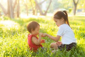 mooie jonge Aziatische jongen zitten spelen in de zomer in het park met genieten en vrolijk op groen gras, kinderen activiteit met ontspanning en geluk samen op weide, familie en vakantie concept. foto