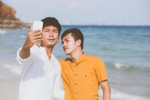 homo portret jong koppel glimlachend nemen van een selfie foto samen met slimme mobiele telefoon op het strand, lgbt homoseksuele minnaar in de vakantie op zee, twee man gaan reizen, vakantie concept.
