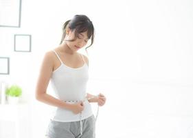 mooie jonge aziatische vrouw lichaamsdieet en slank met het meten van taille voor gewicht in de slaapkamer, meisje heeft cellulitis en calorieënverlies met meetlint, gezondheids- en wellnessconcept. foto