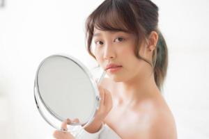 mooi portret jonge aziatische vrouw die spiegel kijkt die make-up lippenstift toepast op kamer, schoonheid lippen azië meisje make-up en cosmetische mode op mond thuis, levensstijl en gezondheidszorg concept. foto