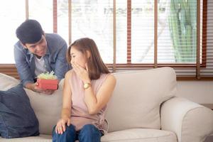 jong aziatisch stel viert samen verjaardag, aziatische man geeft geschenkdoos cadeau aan vrouw voor verrassing in woonkamer, vrouw voelt zich gelukkig en opgewonden verjaardag, valentijnsvakantieconcept. foto