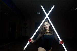 krullend brunette plus size model met twee lange led-lampen op zwarte kamer. foto