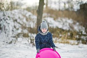 schattig klein meisje met schotel sleeën buiten op winterdag. foto