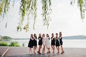 groep van 8 meisjes dragen op zwart en 2 bruiden op vrijgezellenfeest tegen zonnig strand champagne drinken. foto