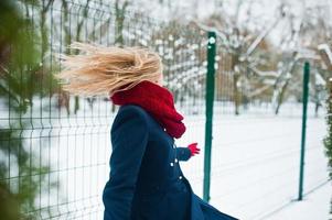 blond meisje in rode sjaal en jas wandelen in het park op winterdag. foto