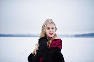 elegantie blond meisje in bontjas en rode avondjurk gesteld op besneeuwde winterdag. foto