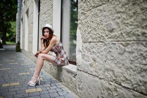 verbazingwekkende lange benen met hoge hakken meisje draagt een hoed zittend op de vensterbank in de straten van de stad. foto