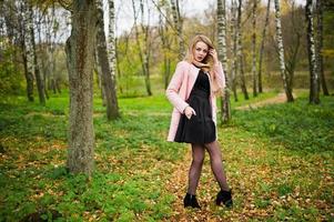 jong blond meisje met roze jas gesteld op herfst park. foto