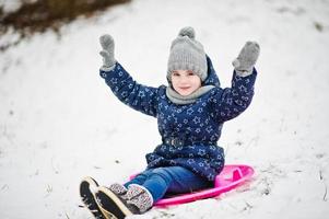 schattig klein meisje met schotel sleeën buiten op winterdag. foto