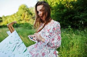 portret van een aantrekkelijke jonge vrouw in lange jurk schilderen met waterverf in de natuur. foto