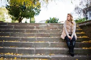 blond meisje op bontjas en bril zittend op trappen met gele bladeren. foto