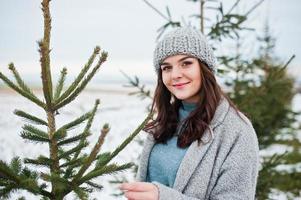 portret van zachtaardig meisje in grijze jas en hoed tegen nieuwjaarsboom buiten. foto