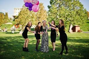 vijf meisjes dragen op zwart met ballonnen rode champagne drinken op vrijgezellenfeest. foto