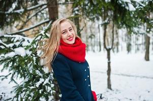 blond meisje in rode sjaal en jas wandelen in het park op winterdag. foto