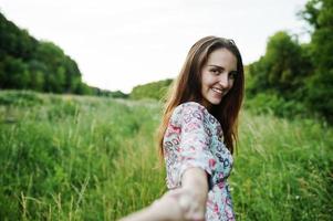 portret van een fantastische jonge vrouw in jurk die in het hoge gras loopt en de hand van haar vriendje vasthoudt. foto