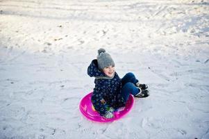 schattig klein meisje met schotel sleeën buiten op winterdag. foto