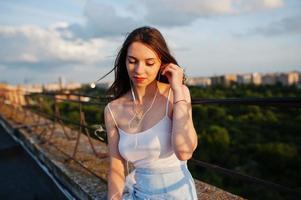 portret van een mooie jonge vrouw in vrijetijdskleding bedekt met witte sjaal of deken zittend op het dak en luisterend naar de muziek. foto