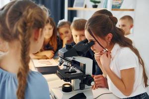 meisje op zoek naar Microscoop. groep kinderen studenten in de klas op school met leraar foto