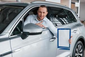 tonen met de wijsvinger. manager zit in moderne witte auto met papier en documenten in handen foto