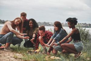 laat de vlam niet uitgaan. groep mensen hebben picknick op het strand. vrienden veel plezier in het weekend foto