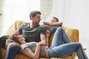 kind leunend op de bank. gelukkige familie veel plezier op de gele bank in de woonkamer van hun nieuwe huis foto