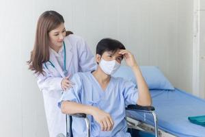aziatische doktersvrouw die praat met een man-patiënt die een gezichtsmasker draagt over zijn gezondheidssymptoom terwijl hij in een rolstoel in het ziekenhuis zit. foto