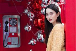 Aziatische mooie vrouw langharig draagt een geel gewaad en glimlachend gelukkig staande voor een rode telefooncel in het thema van het vieren van kerstmis en gelukkig nieuwjaar foto