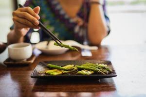 vrouw grill asperges eten met houten stokjes in restaurant. foto