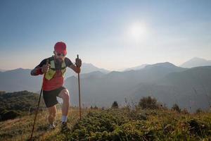 man atleet van sky-raid in de bergen met stokken stokken bergop foto