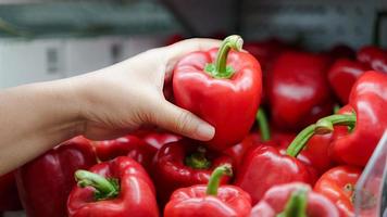 close-up vrouw hand met verse rode paprika op de plank bij supermarkt. foto