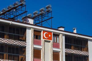 side turkije 01 maart 2022 laag huis met nationale vlag van turkije, vaten warm water op het dak en zonnepanelen foto