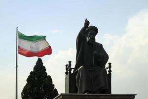 teheran, iran - 10 juni 2018 - een grote iraanse vlag die in de wind zwaait achter een standbeeld van khomeini in teheran, iran foto