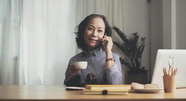 gelukkige vrij rijpe vrouw die op mobiel telefoonportret spreekt. senior grijsharige dame die telefoneert, thuis op de bank zit, geniet van praten, communicatie, camera kijken, glimlachen foto